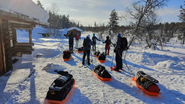 Matkajad suuskade ja pulkadega lumisel platsil puumaja juures Lapimaal